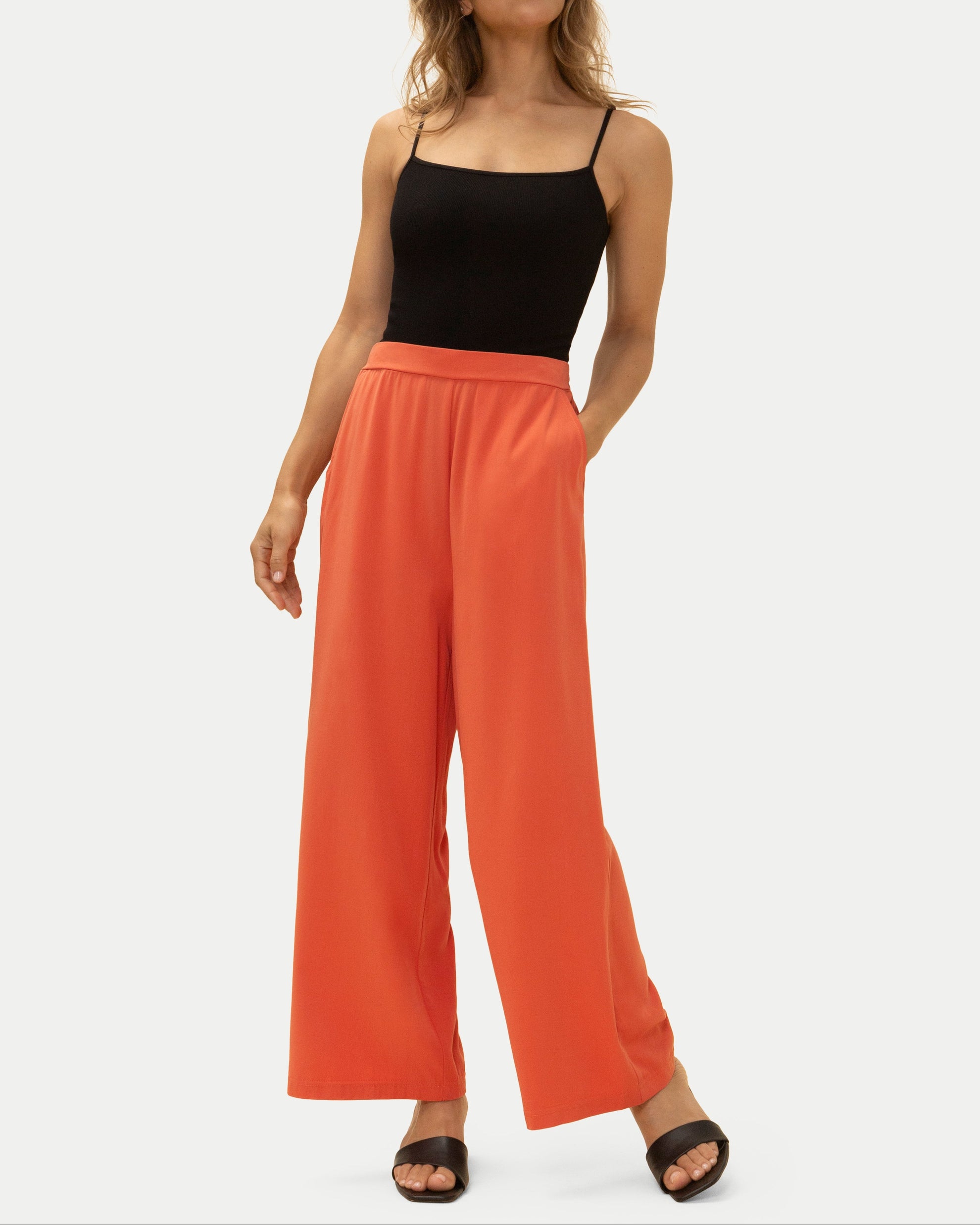 Woman wearing orange wide-leg pants and a black top on a white background