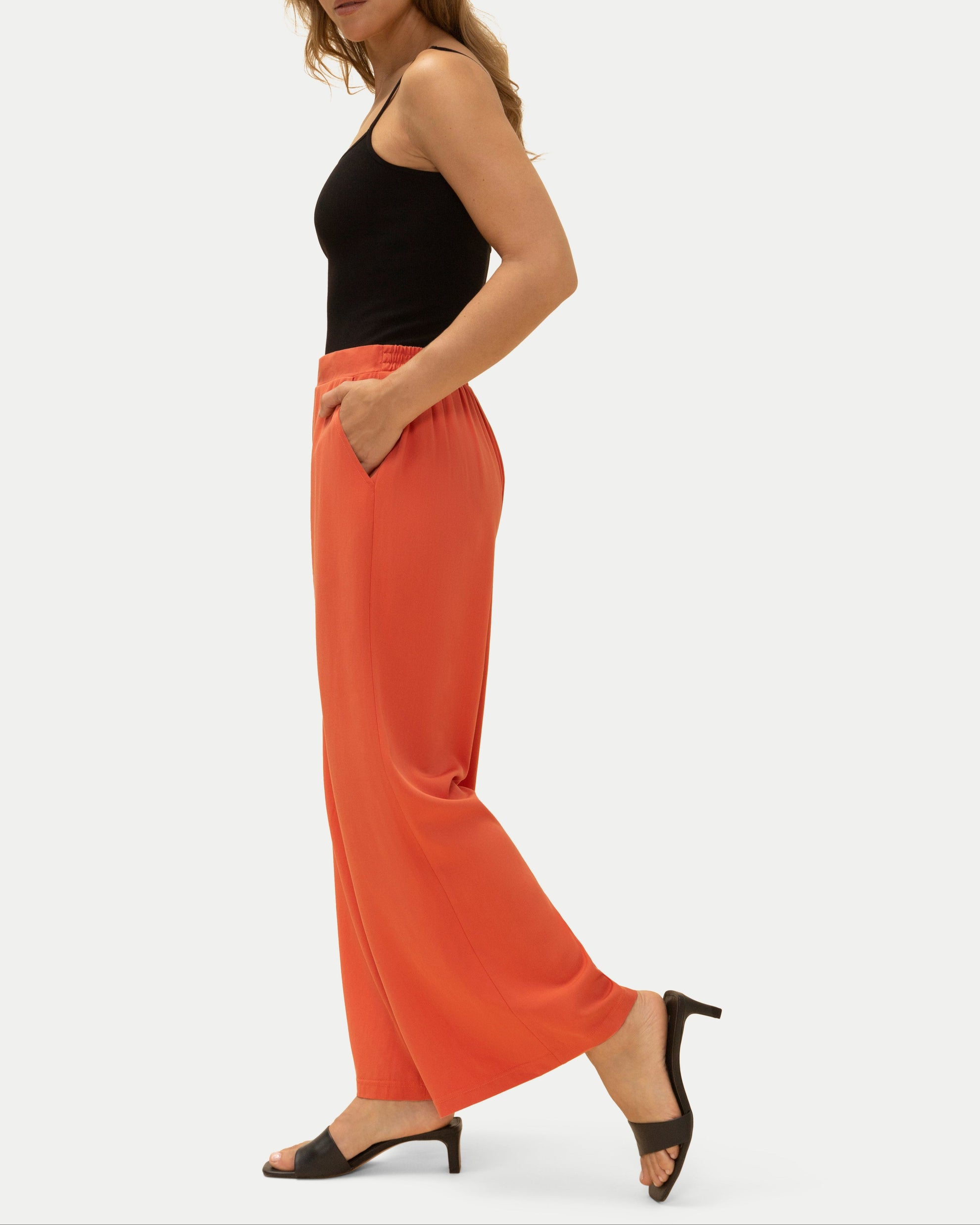 Woman wearing a black top and orange pants on a white background