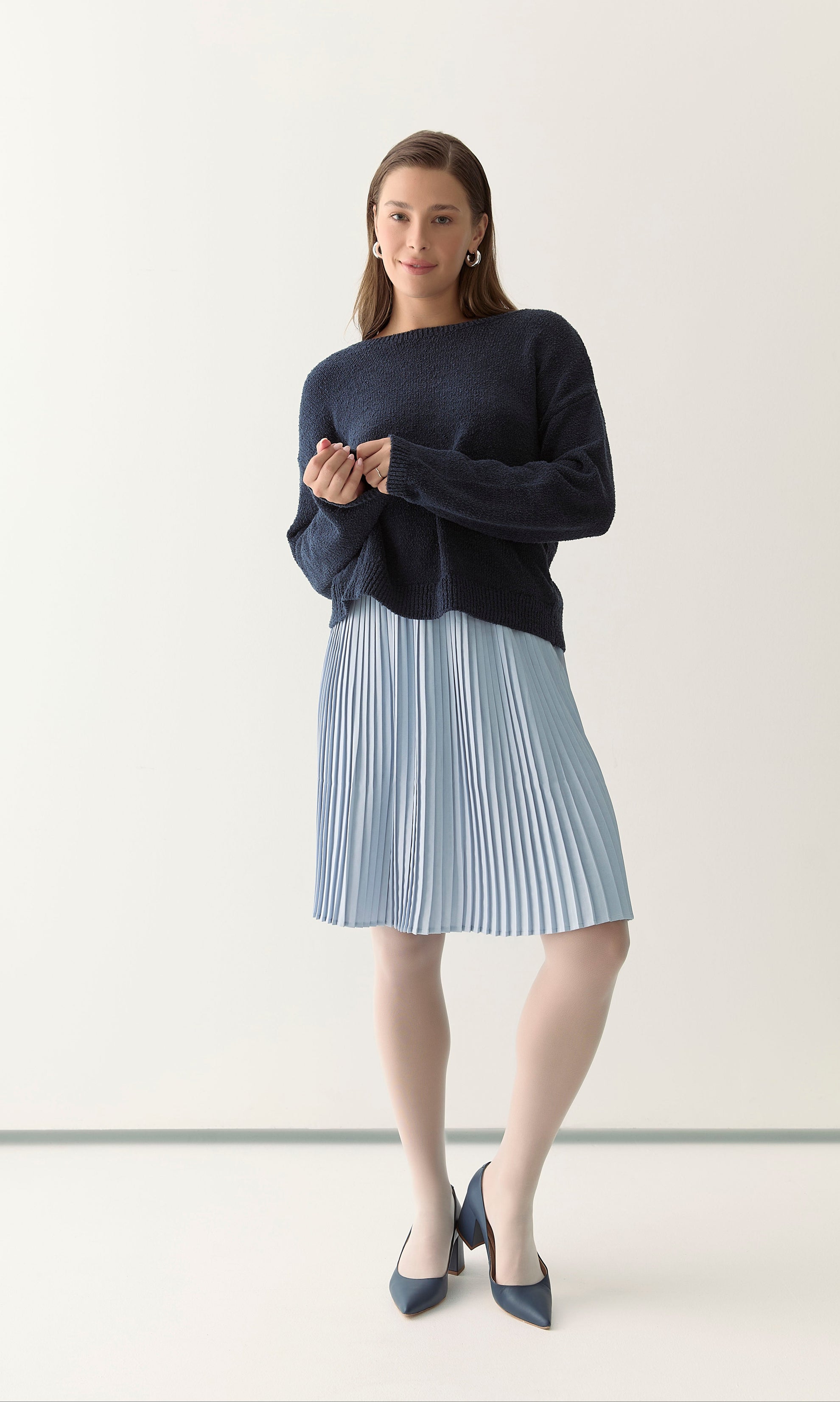 Woman wearing a navy sweater and light blue pleated skirt 