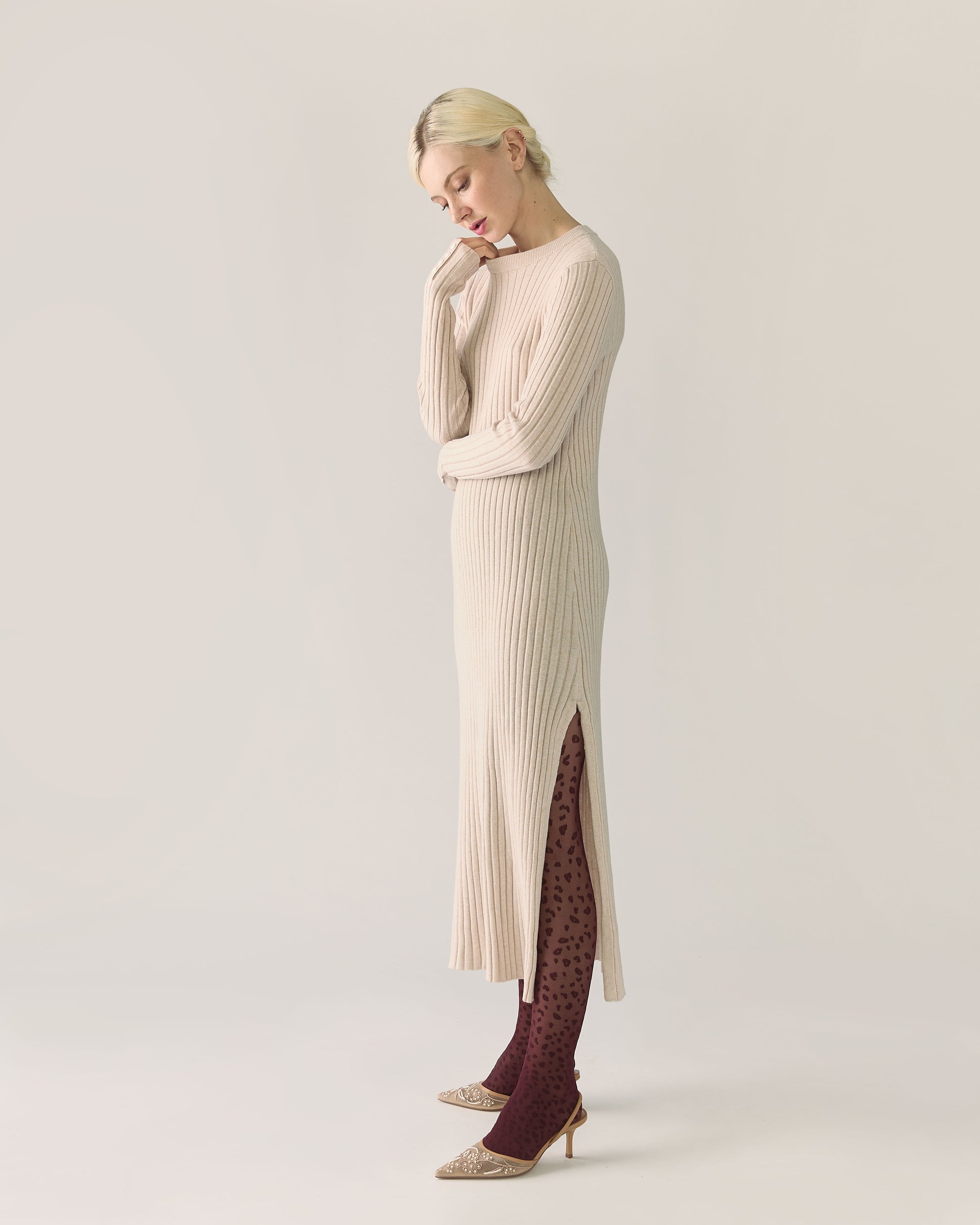 Woman wearing a long beige ribbed sweater dress with a slit