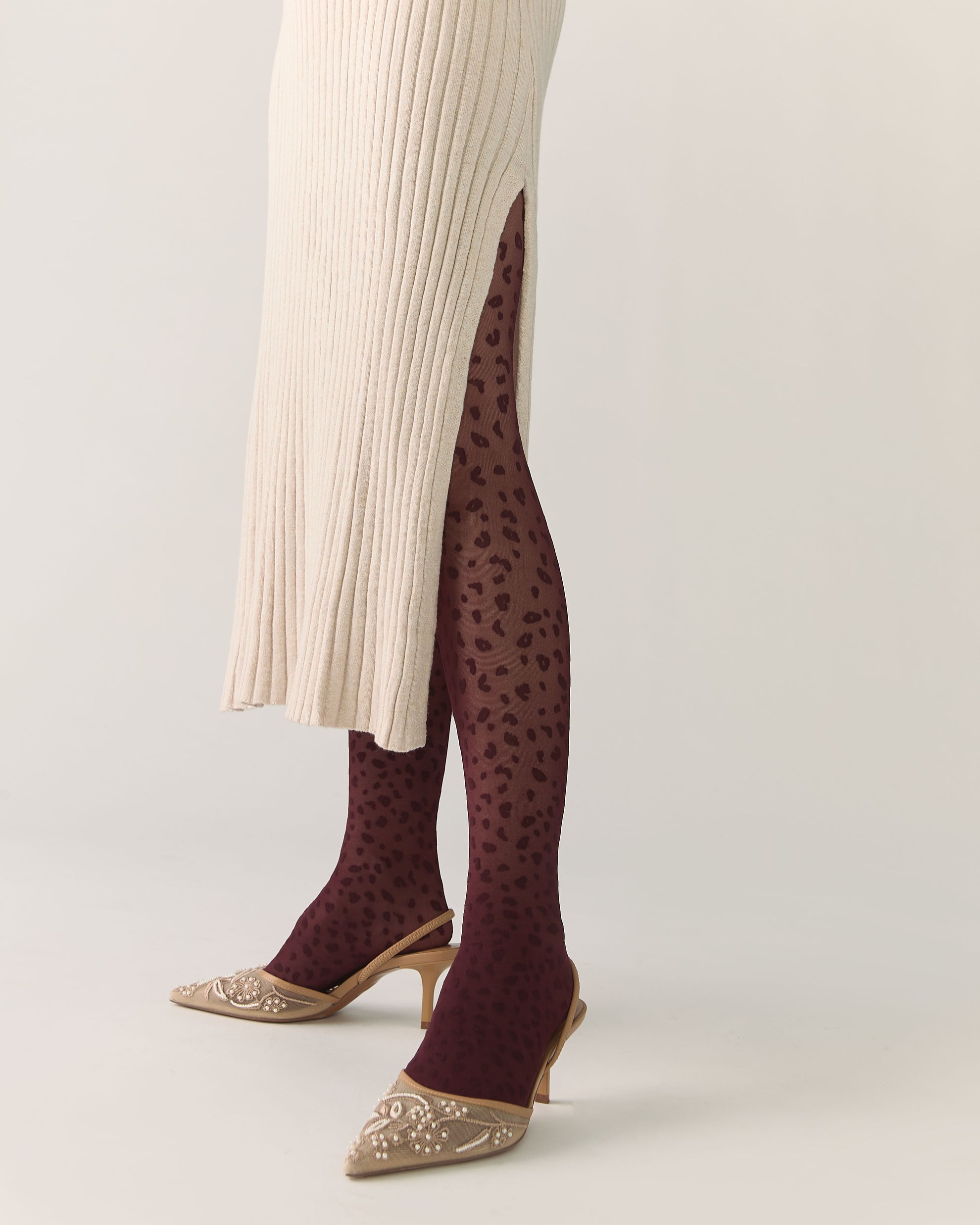 Person wearing burgundy patterned animal print tights with beige high heels and sweater dress