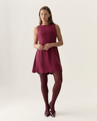 Woman wearing a maroon dress with patterned tights on a white background