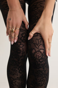 Hands adjusting the Floral Lace tights in Black at the thigh, showing the delicate lace pattern up close.