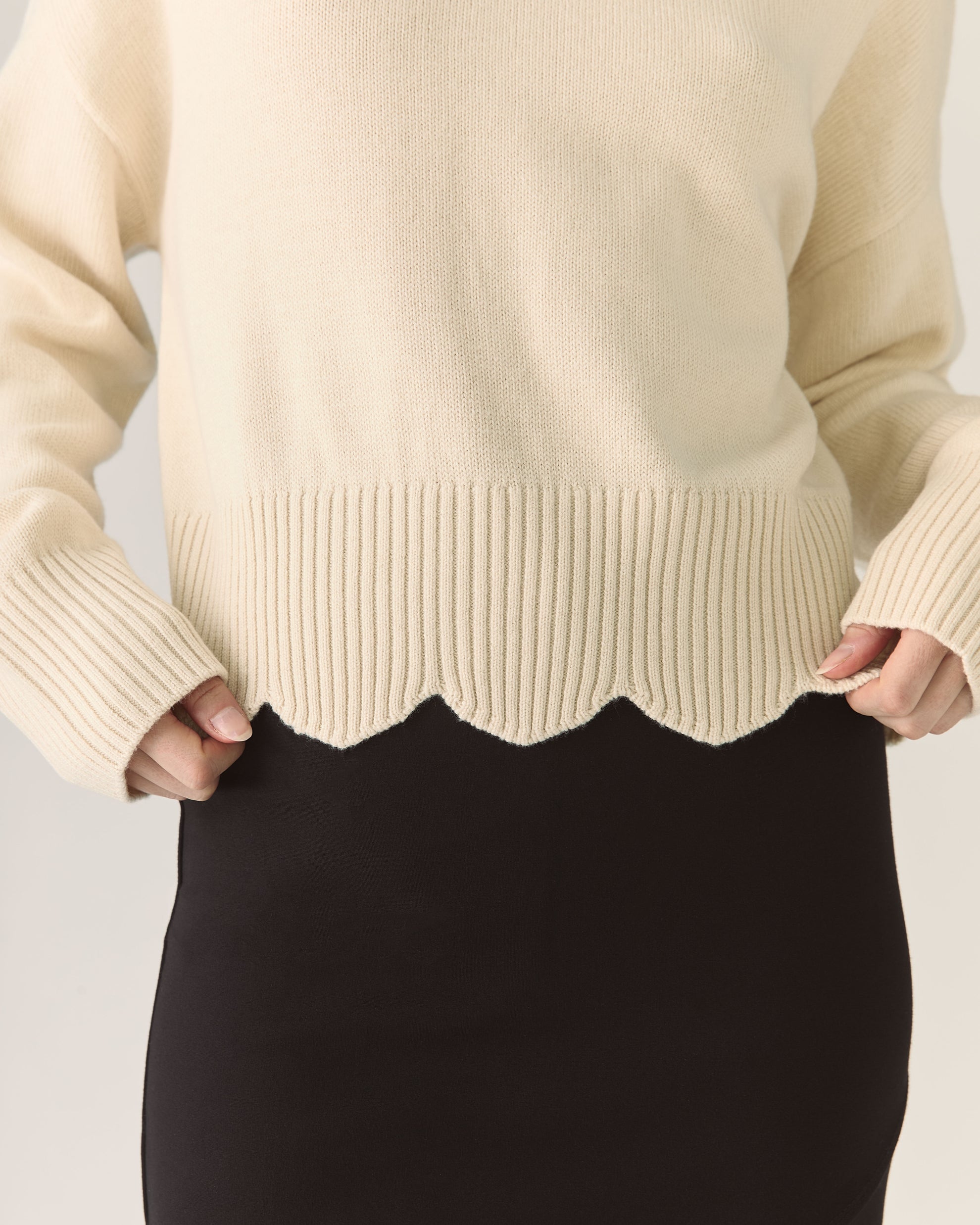Beige sweater with scalloped hem worn by a person on a light background