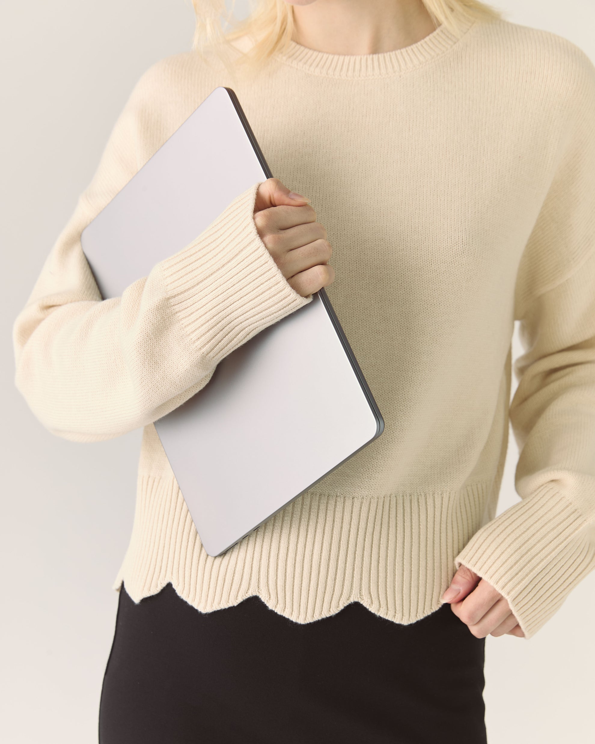 Person wearing a beige sweater holding a light gray laptop against a plain background