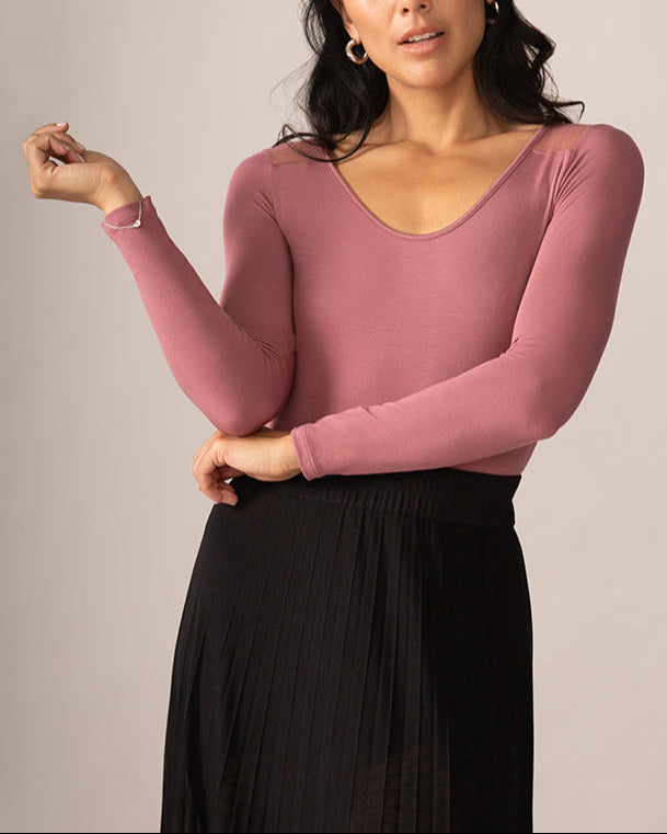 Woman wearing a pink long-sleeve top and black skirt against a neutral background