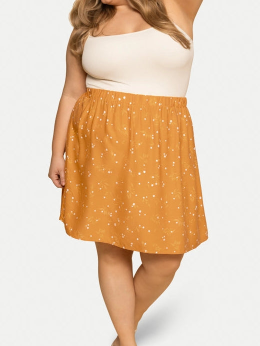 Woman wearing a white top and mustard yellow skirt with white patterns on a white background