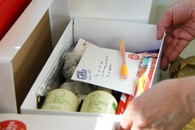 Open box containing various items including a pen, toothbrushes, and a bottle labeled 'Tea Tree Soap'.
